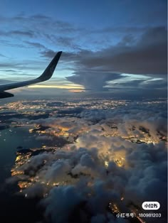 the wing of an airplane flying over clouds at night with city lights in the distance