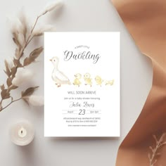 a white card with ducks on it next to a candle and some dried flowers in the background