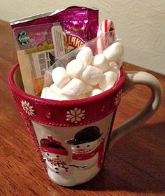 a cup filled with marshmallows and candy on top of a wooden table