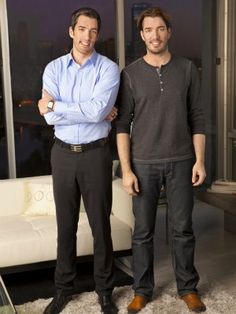 two men standing next to each other in front of a living room with large windows