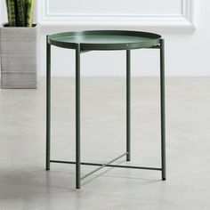 a green table with a potted plant in the corner next to it on a concrete floor