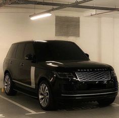 a black range rover is parked in a parking garage with white walls and ceiling lights