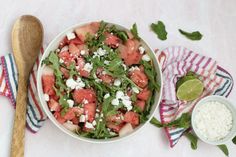 a watermelon salad with feta cheese and basil in a bowl next to a wooden spoon