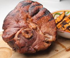 a large piece of meat sitting on top of a wooden cutting board next to a bowl of fries