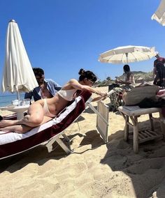 a woman laying on top of a red and white beach chair next to an umbrella