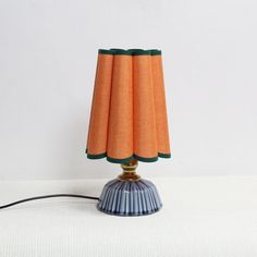 an orange and blue table lamp on a white surface with a black cord attached to it