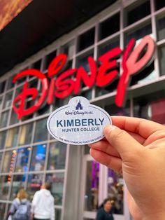 someone holding up a sticker in front of a building with the disney logo on it