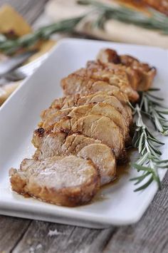 some meat is sitting on a white plate with rosemary sprigs and sauce in front of it