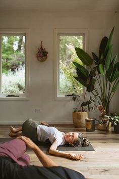 two people laying on their stomachs in the middle of a yoga studio with large windows