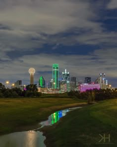 the city skyline is lit up in green and purple at night, as well as water