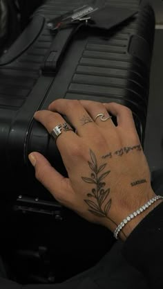 a person's hand with tattoos on their fingers next to a black suitcase,