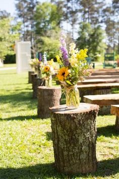 flowers are in a vase on top of a tree stump at a wedding ceremony outside