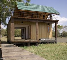 a small house built on stilts in the middle of a field with a green roof