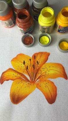 an orange flower is painted on a white table cloth with several different colors of paint