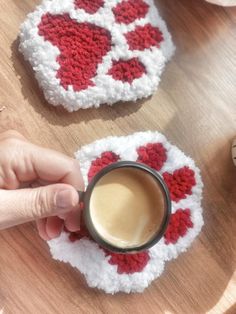 two crocheted coasters with hearts on them, one holding a cup of coffee