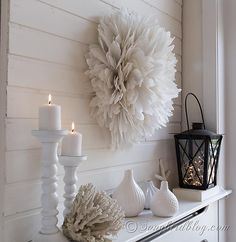 a white mantle topped with candles and a large paper flower on top of it's mantle