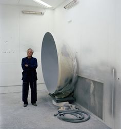 a man standing next to a large object in a room with white walls and floors