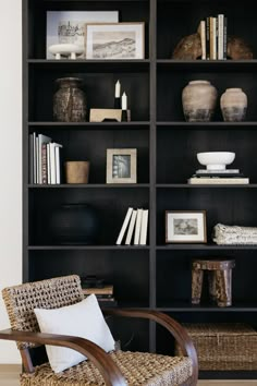 a black bookcase filled with lots of books next to a wicker chair and vases