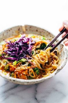 someone is holding chopsticks over a bowl of noodles and veggies with sauce