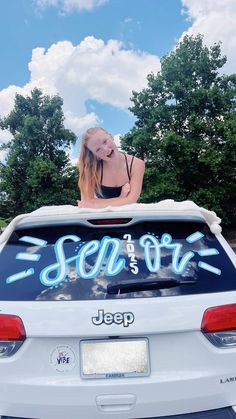 a woman sticking her head out of the back of a car that is parked in front of some trees