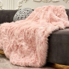 a couch with a pink blanket on top of it next to a gray pillow and two pillows