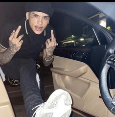 a man sitting in the driver's seat of a car with his hands up