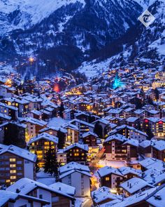 the city is covered in snow and lit up at night with mountains in the background