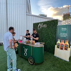 people are standing around at an outdoor bar with drinks on the table and behind it is a sign that says oasis