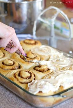 someone cutting into some cinnamon rolls in a pan