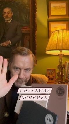 a man sitting in a chair with his hand up to the camera and two books stacked on top of him