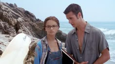 a young man and woman standing next to each other near the ocean with surfboards