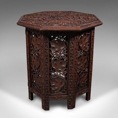 an intricately carved wooden table with carvings on the top and bottom, sitting against a gray background