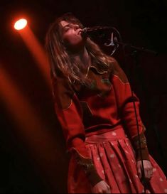 a woman in a red dress singing into a microphone on stage with lights behind her