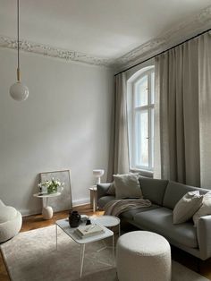 a living room filled with furniture and a large window covered in curtains next to a white rug