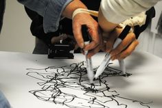 two people are drawing on a white sheet with black ink and scissors in their hands