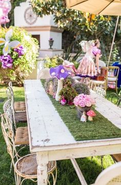 an outdoor table with flowers and fairy figurines on the grass in front of it