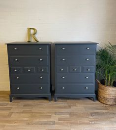 two black dressers side by side in front of a white brick wall and potted plant