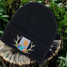 a black beanie with deer antlers is sitting on a stump in the grass