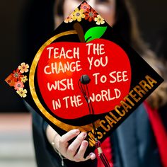 a woman holding up a graduation cap that says teach the change you wish to see in the world