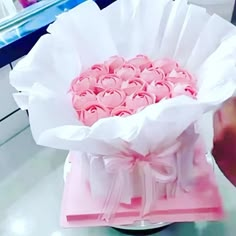 a pink box filled with lots of roses on top of a white counter next to a person's hand