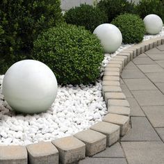 some white balls and rocks in the middle of a garden with plants around them on either side of a brick walkway