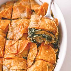 a casserole dish with spinach, cheese and sauce in it on a white table