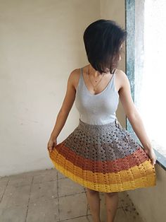 a woman standing next to a window wearing a multicolored skirt and white tank top