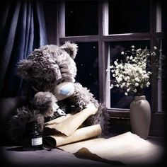 a teddy bear sitting on top of papers next to a vase with flowers in it