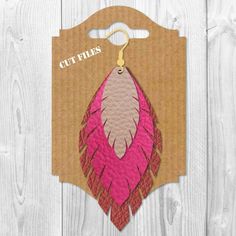 a pink and brown leather feather shaped bag tag on a wooden background with the text cut files