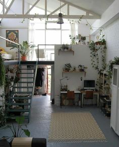 a room filled with lots of plants next to a white brick wall and stairs leading up to the second floor