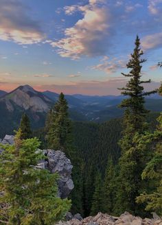 the sun is setting in the mountains with pine trees and rocks on the ground below