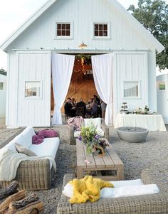 a group of people standing in front of a white barn with lots of furniture and decor