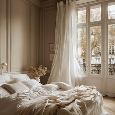 an unmade bed with white sheets and pillows in front of a large open window