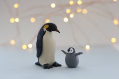 a penguin and its chick standing next to each other in front of a christmas tree